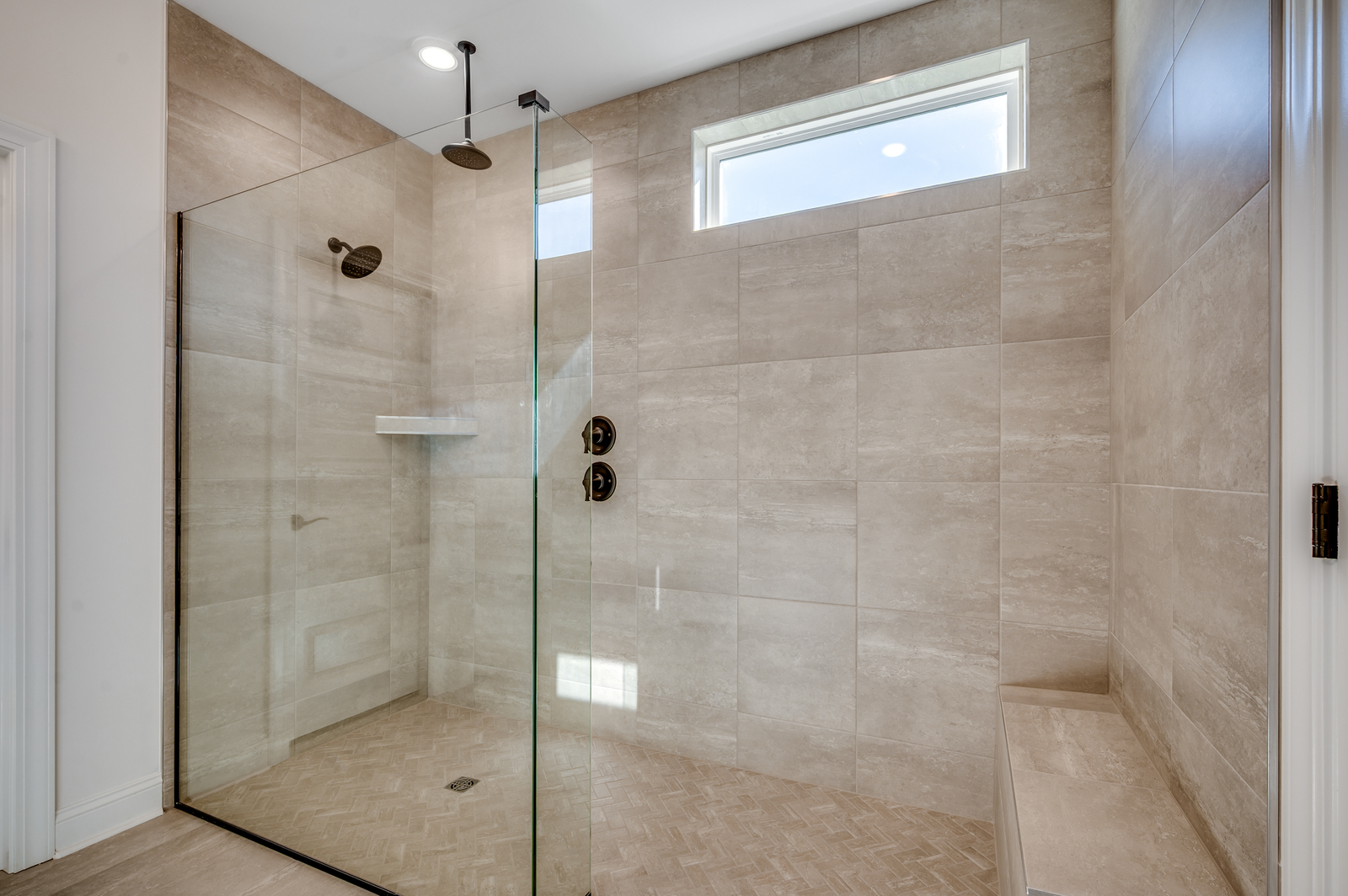 spacious walk-in shower with large glass door, seating area and tiled walls and flooring throughout