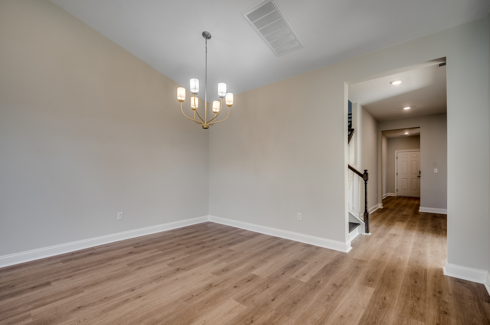 spacious room with tan walls, hardwood flooring and gold chandelier