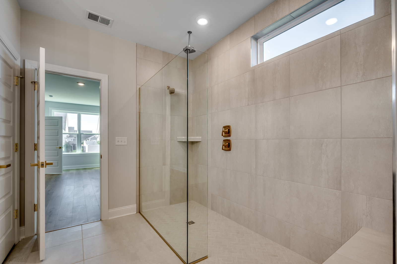 spacious spa-inspired walk-in shower with gold hardware, tiled flooring and tiled walls