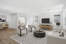 open-concept space with large neutral colored couch, beige rug and black ottoman