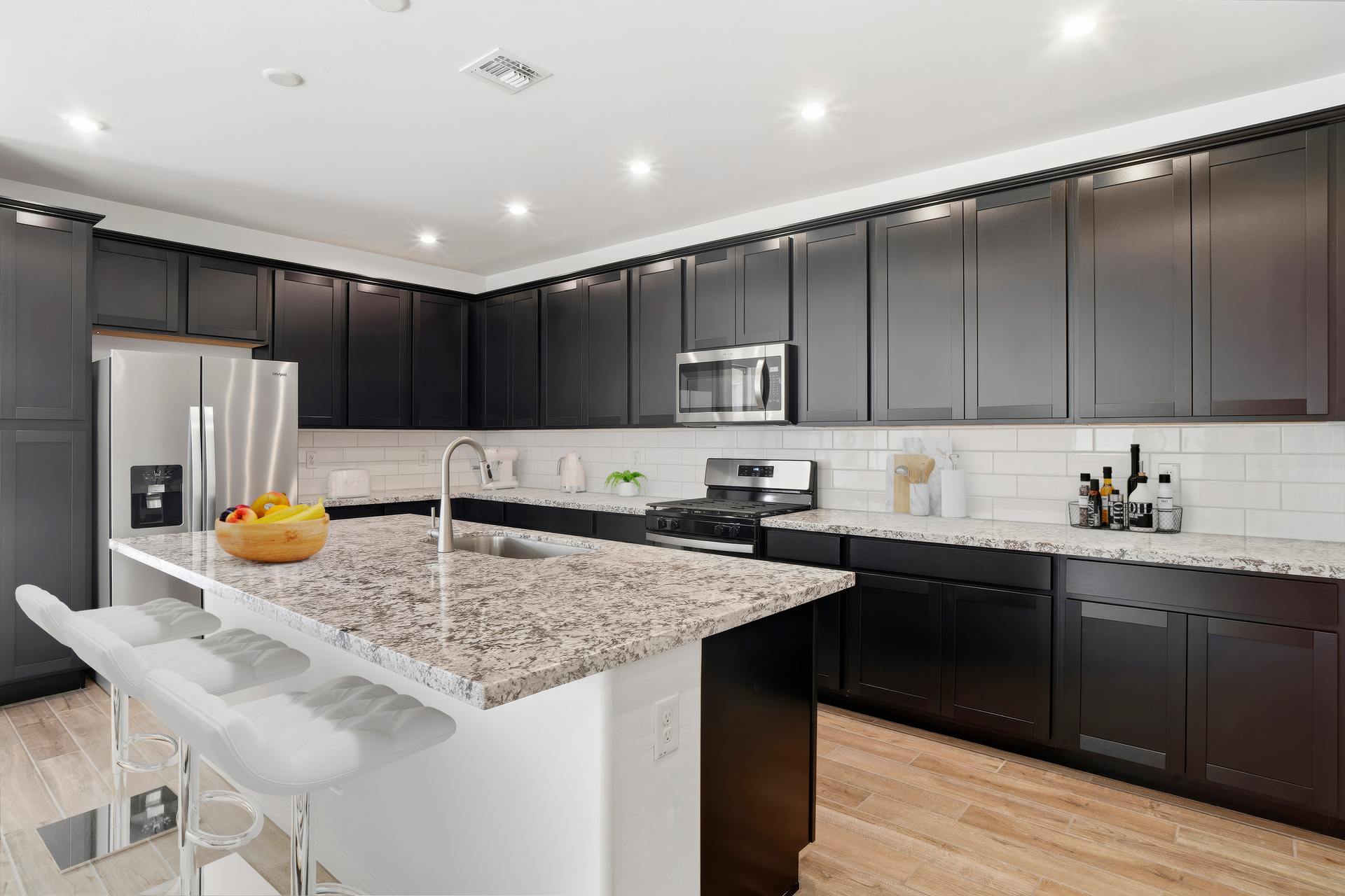 open-concept kitchen with granite countertops, black cabinets, and white barstools