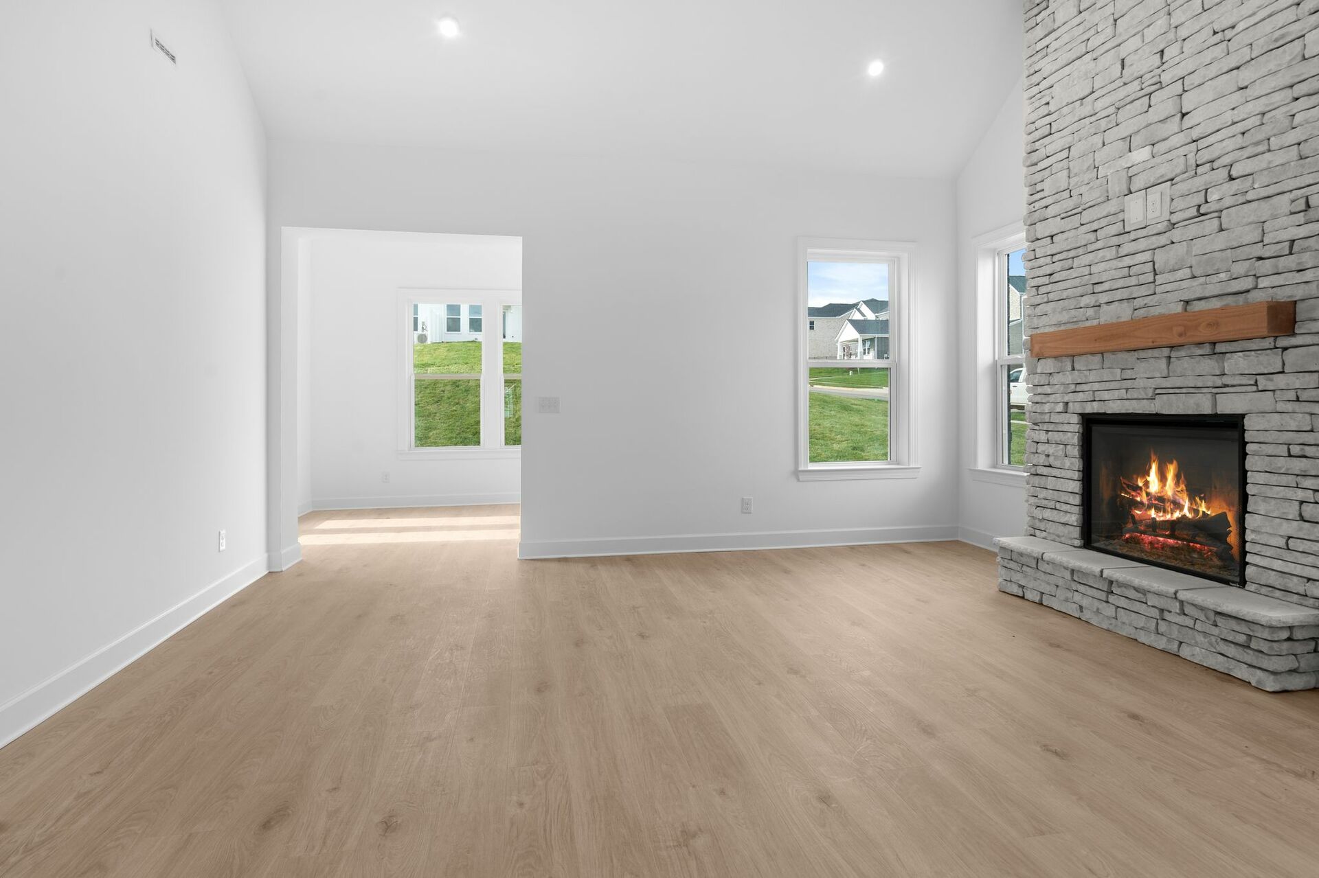 great room with wood flooring, vaulted ceiling, and stone fireplace