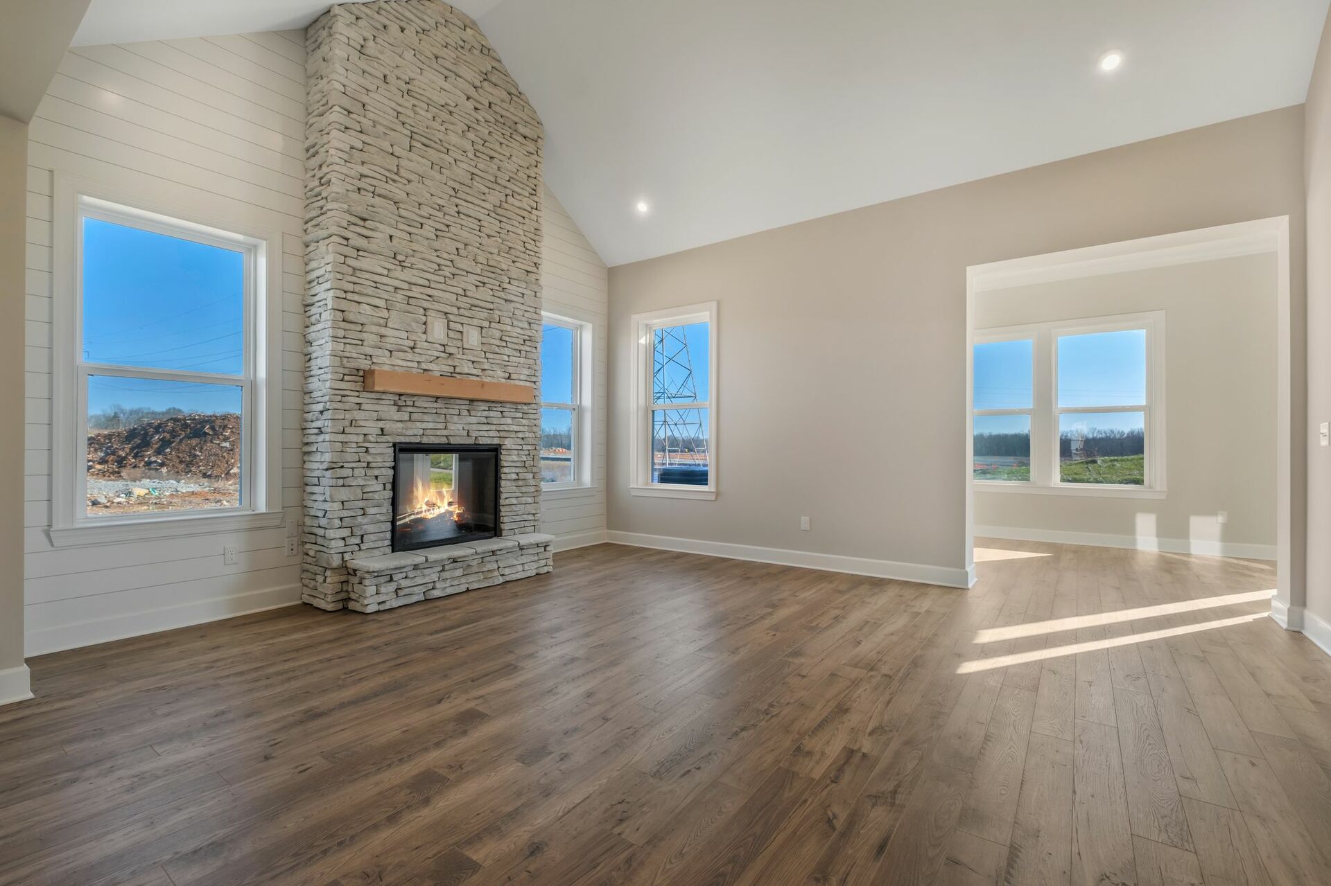 great room with wood floors, a stone fireplace, and vaulted ceilings