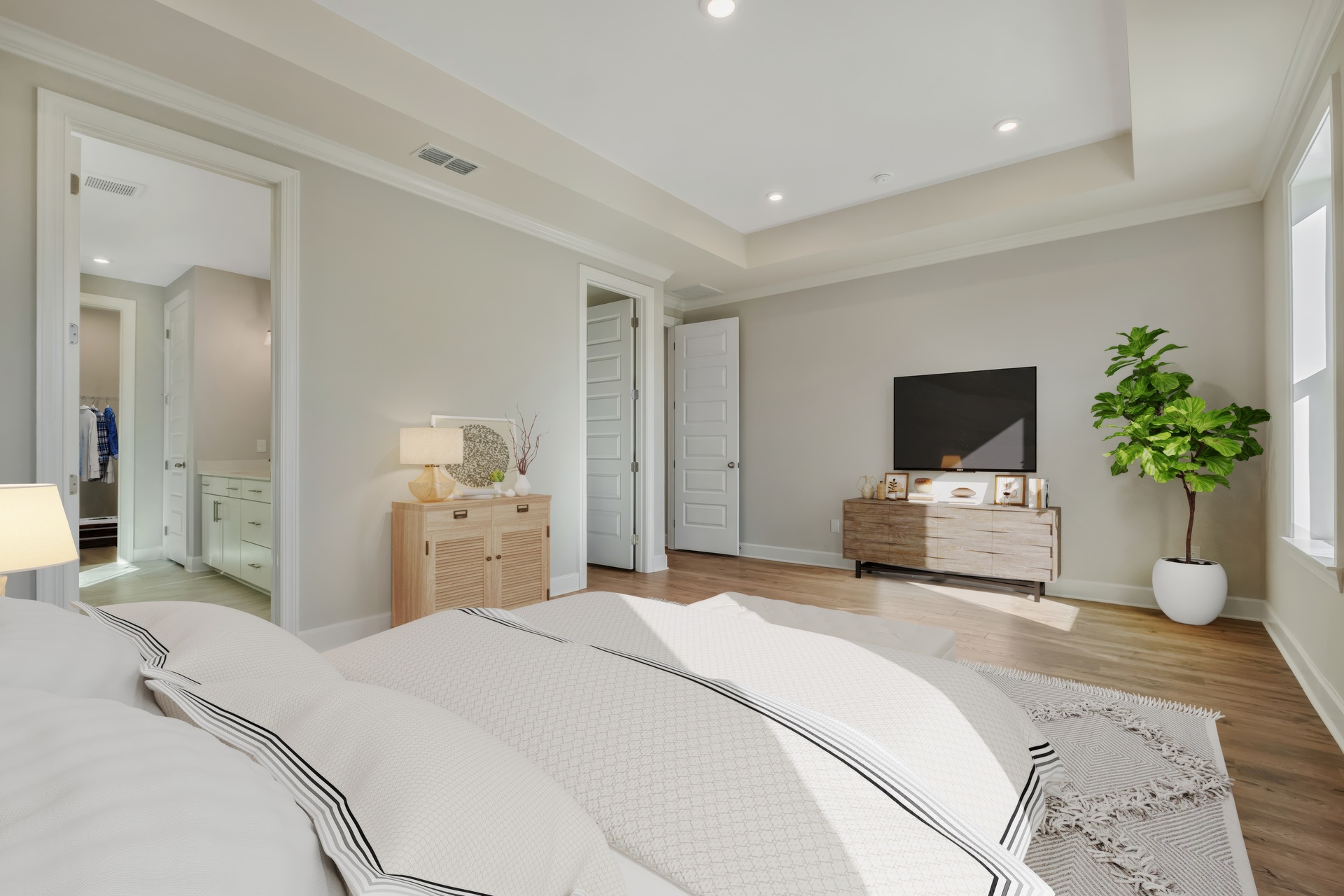 primary bedroom with wood flooring, a tray ceiling, and a view of the bathroom