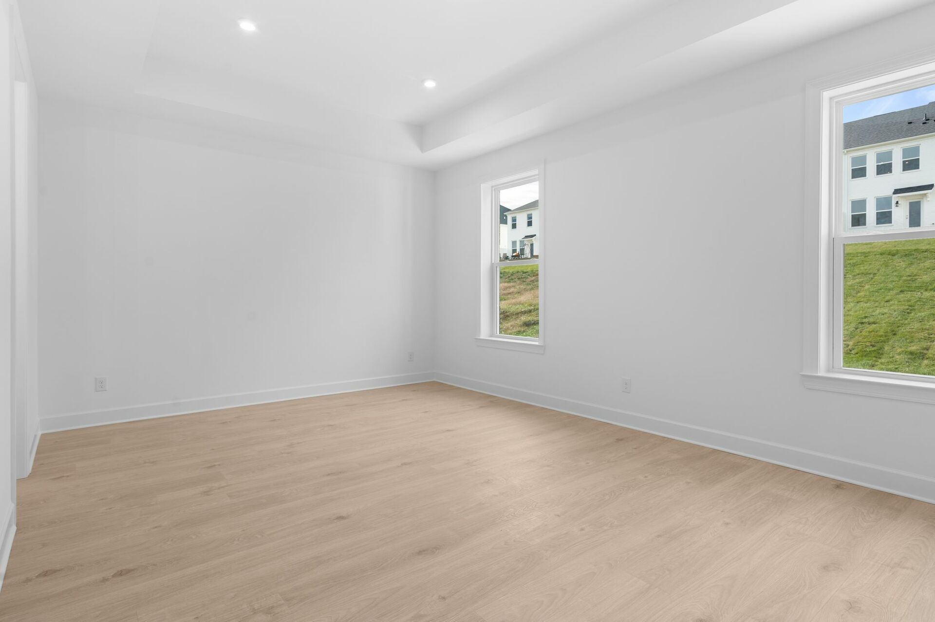 primary bedroom with wood flooring, tray ceiling, and large windows