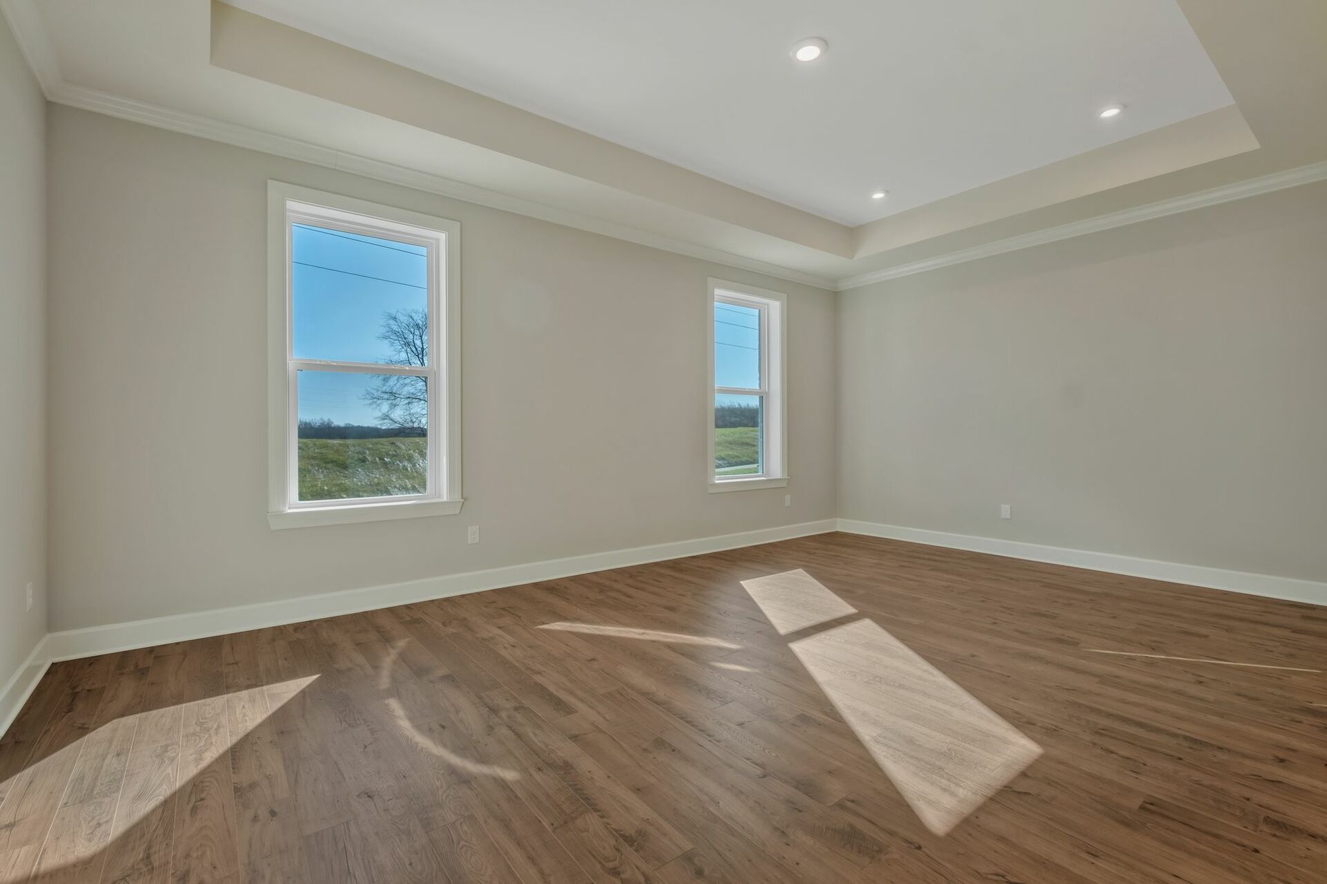 primary bedroom with wood flooring, a tray ceiling, and large windows