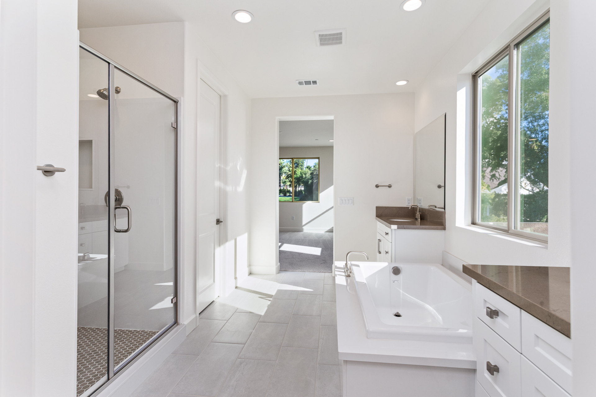 primary bathroom with white cabinets and large window