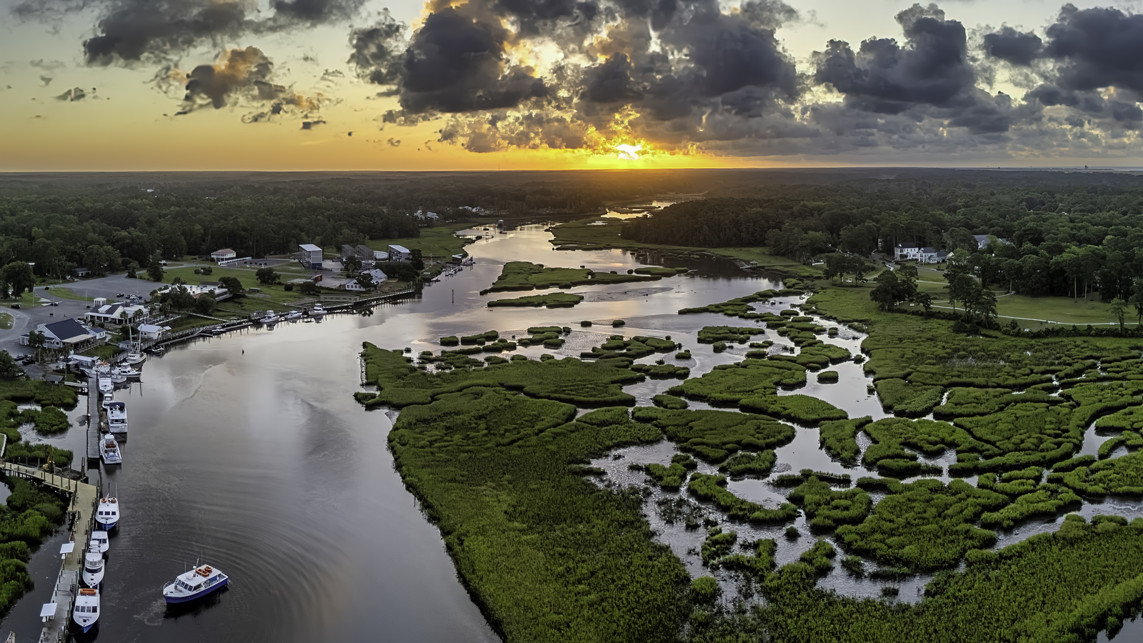 Boats on calm Little River waters at sunset over the marsh