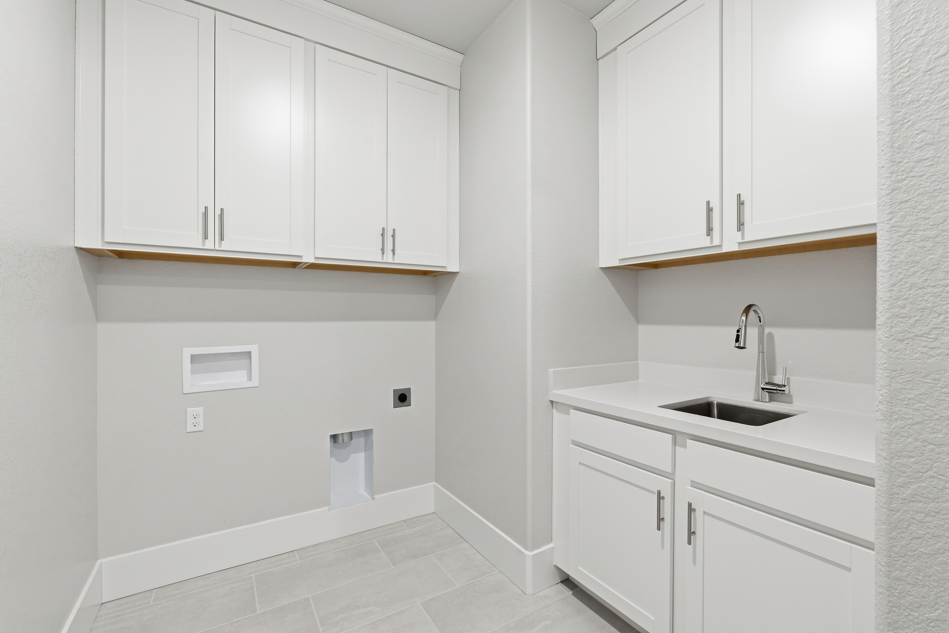 laundry room with white upper & lower cabinets, sink, and tile floors