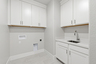 laundry room with white upper & lower cabinets, sink, and tile floors