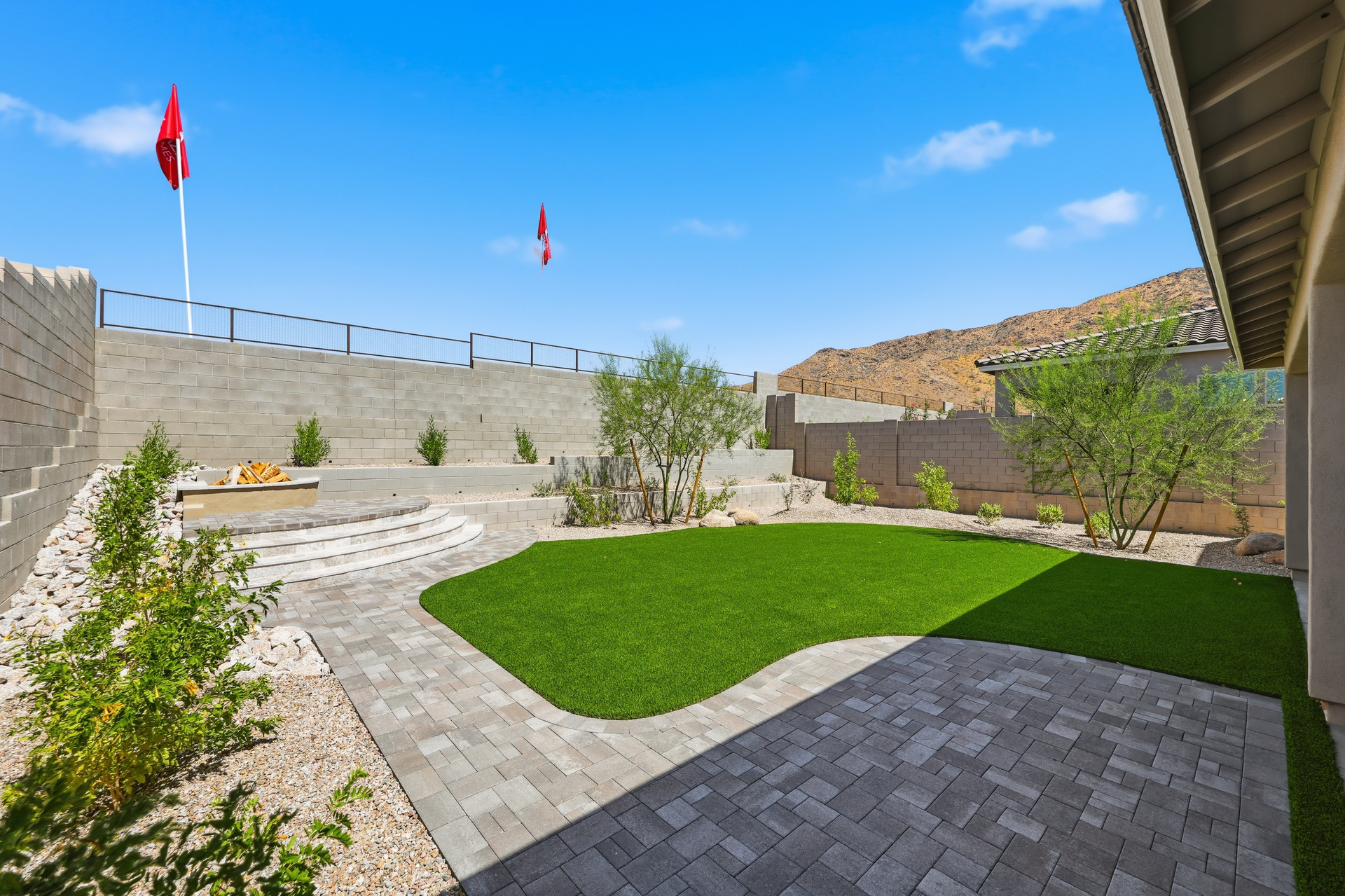 spacious backyard with pavers, artificial grass, and elevated space with a fire pit