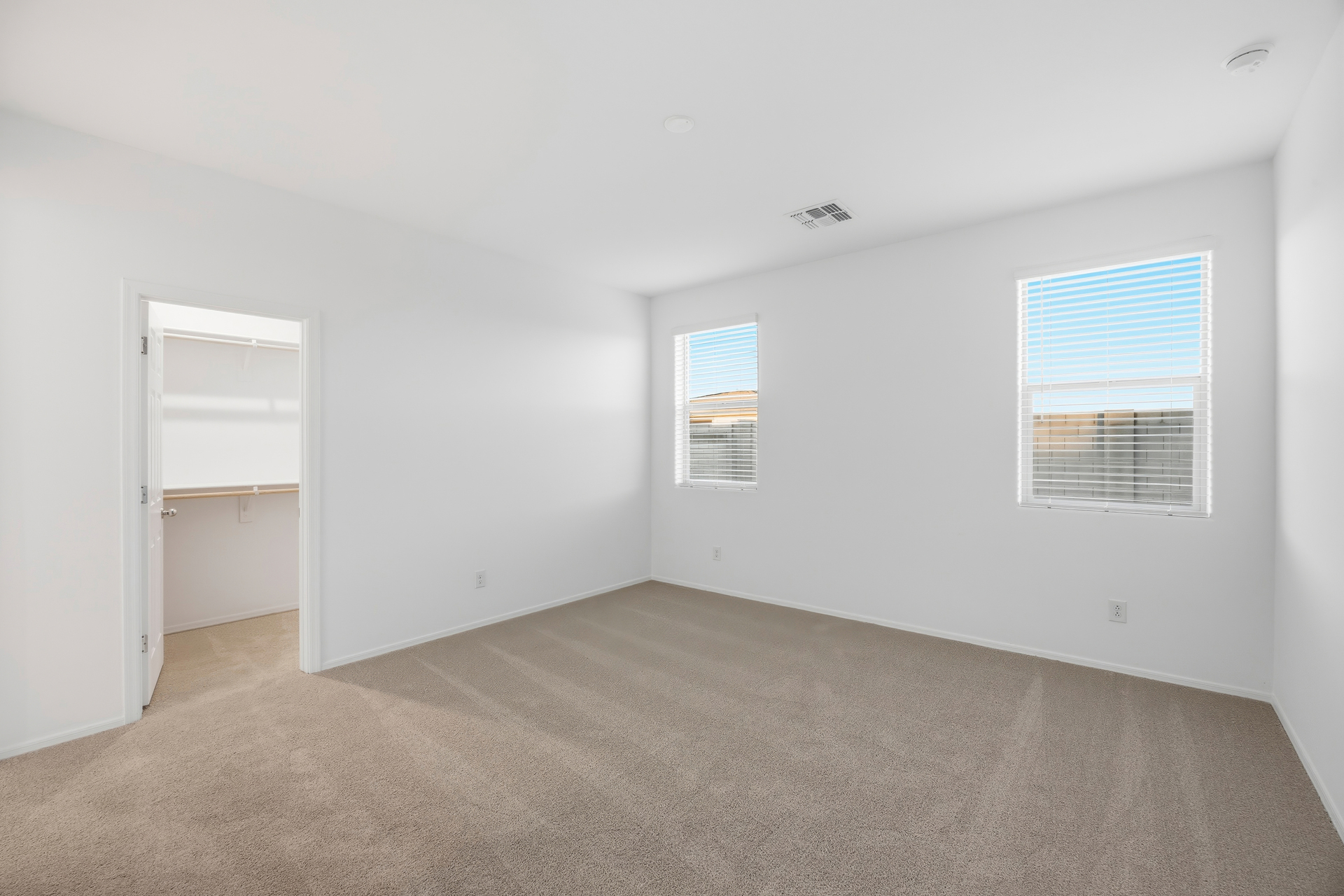 spacious bedroom with light brown carpet and windows for natural light