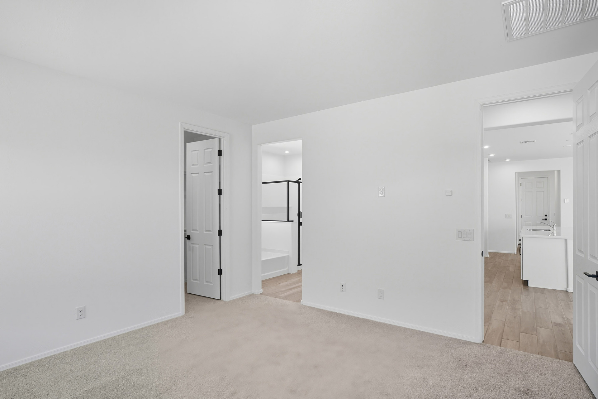 spacious bedroom with light grey carpet and doors leading to the primary bathroom and great room