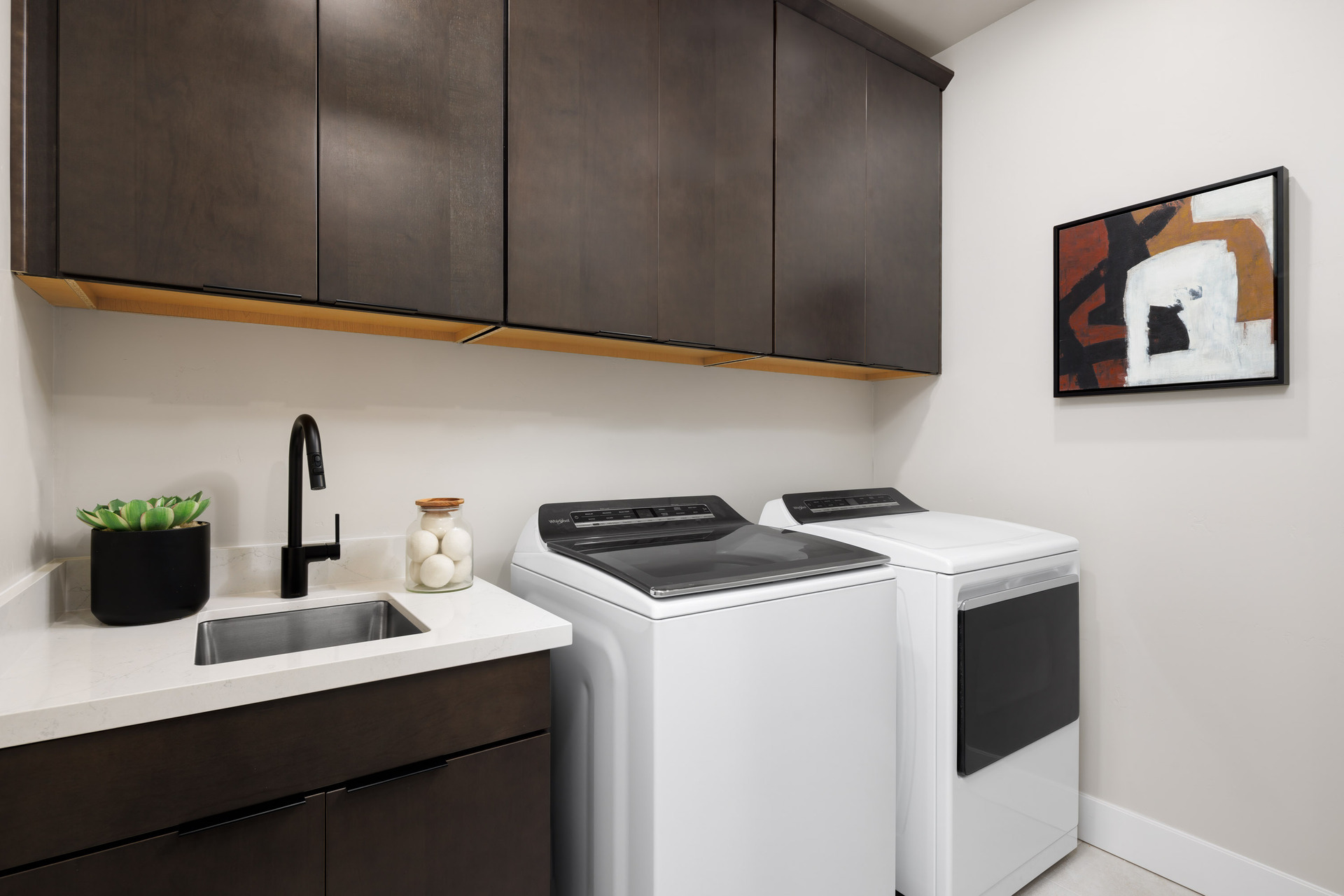laundry room with espresso cabinets, white washer & dryer, and sink