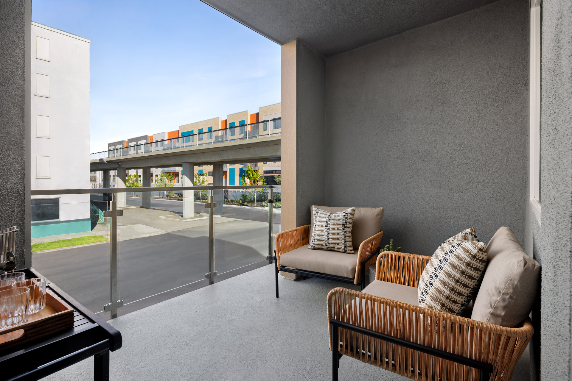 outdoor covered deck with two rattan chairs, bar cart with drinking glasses, and view of street and other buildings