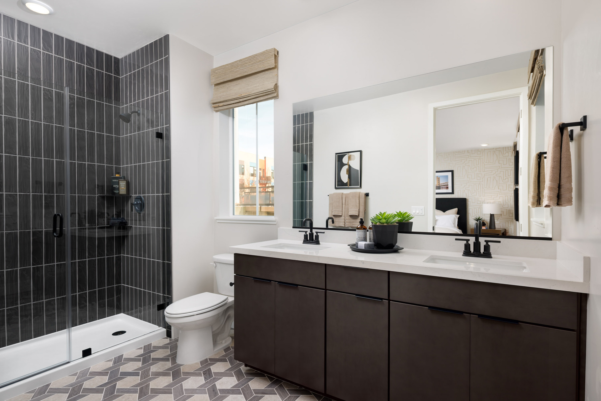 bathroom with espresso cabinets, white counters, two sinks, black tiled walk-in shower, and window above toilet