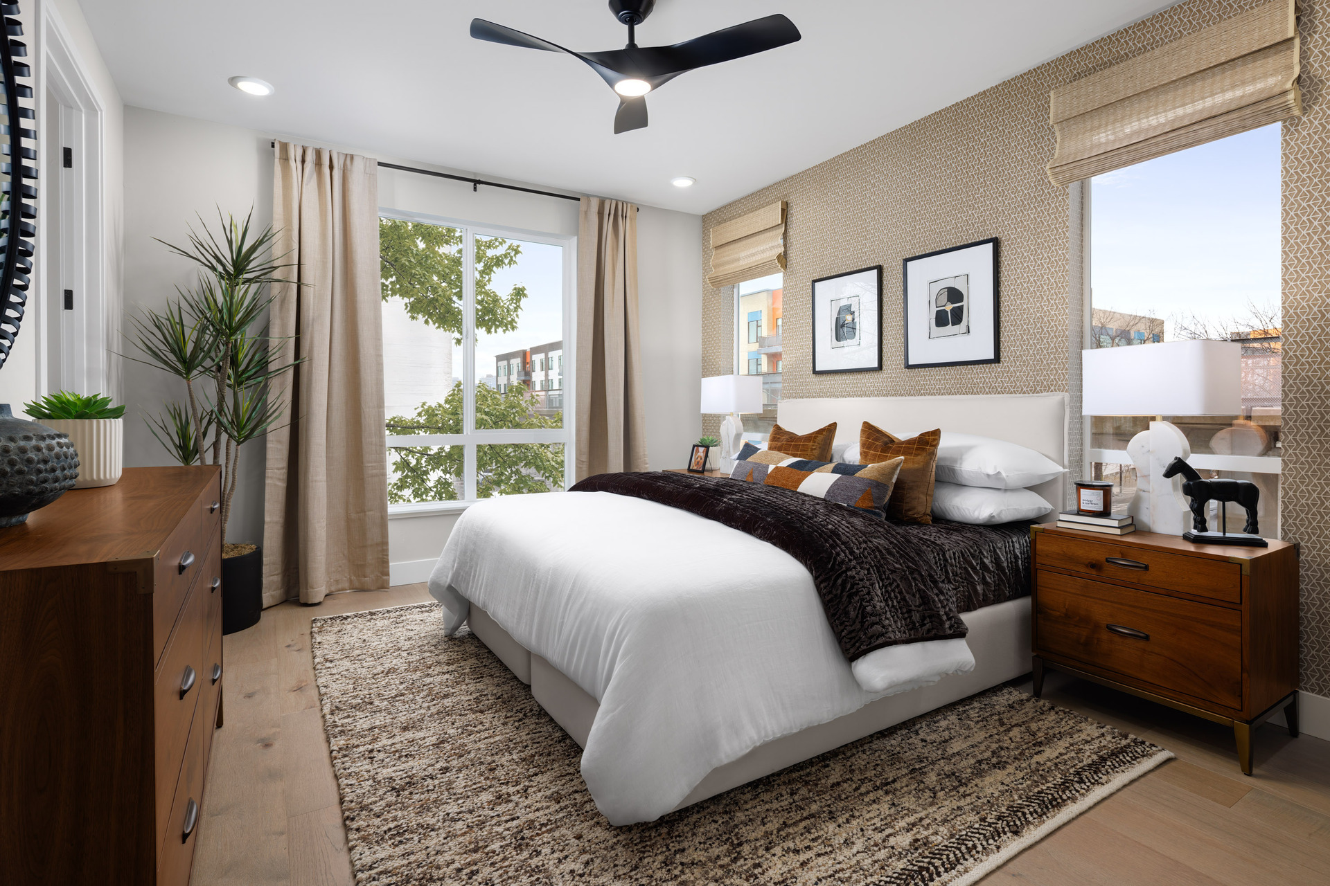 bedroom with wood floors, tan patterned wallpaper behind white upholstered bed, wood dresser, and three windows