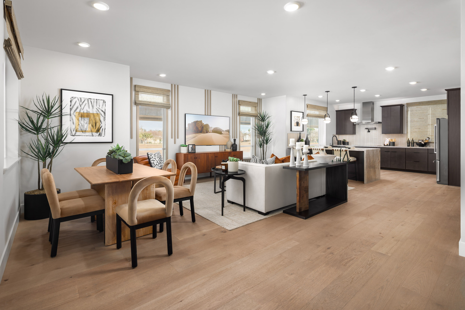 great room with wood floors, white sofa with orange pillows, wood console table under television, multiple windows, and wood dining table