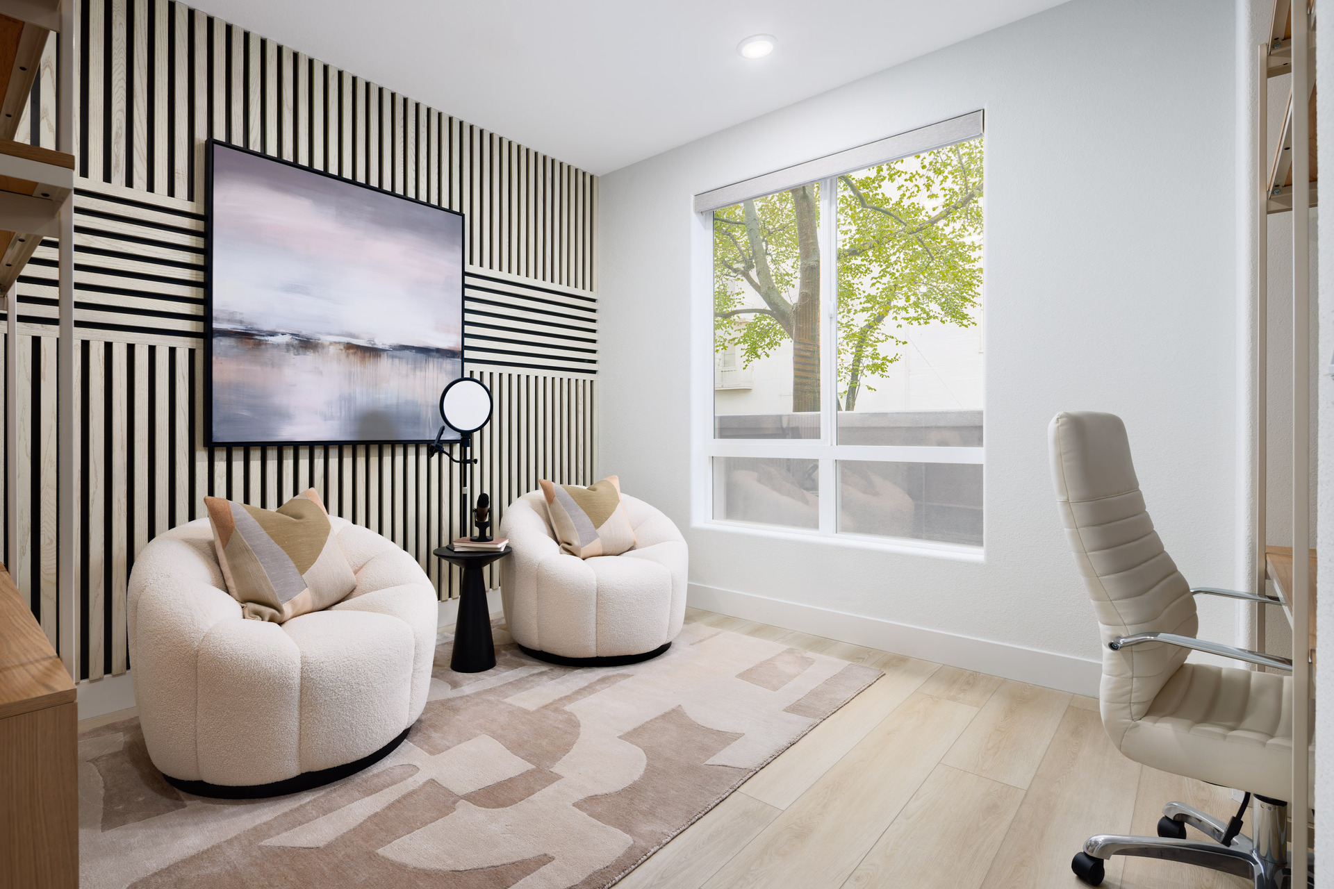 study with light wood floors, modern wood accent wall, two white club chairs, and window looking out to front patio