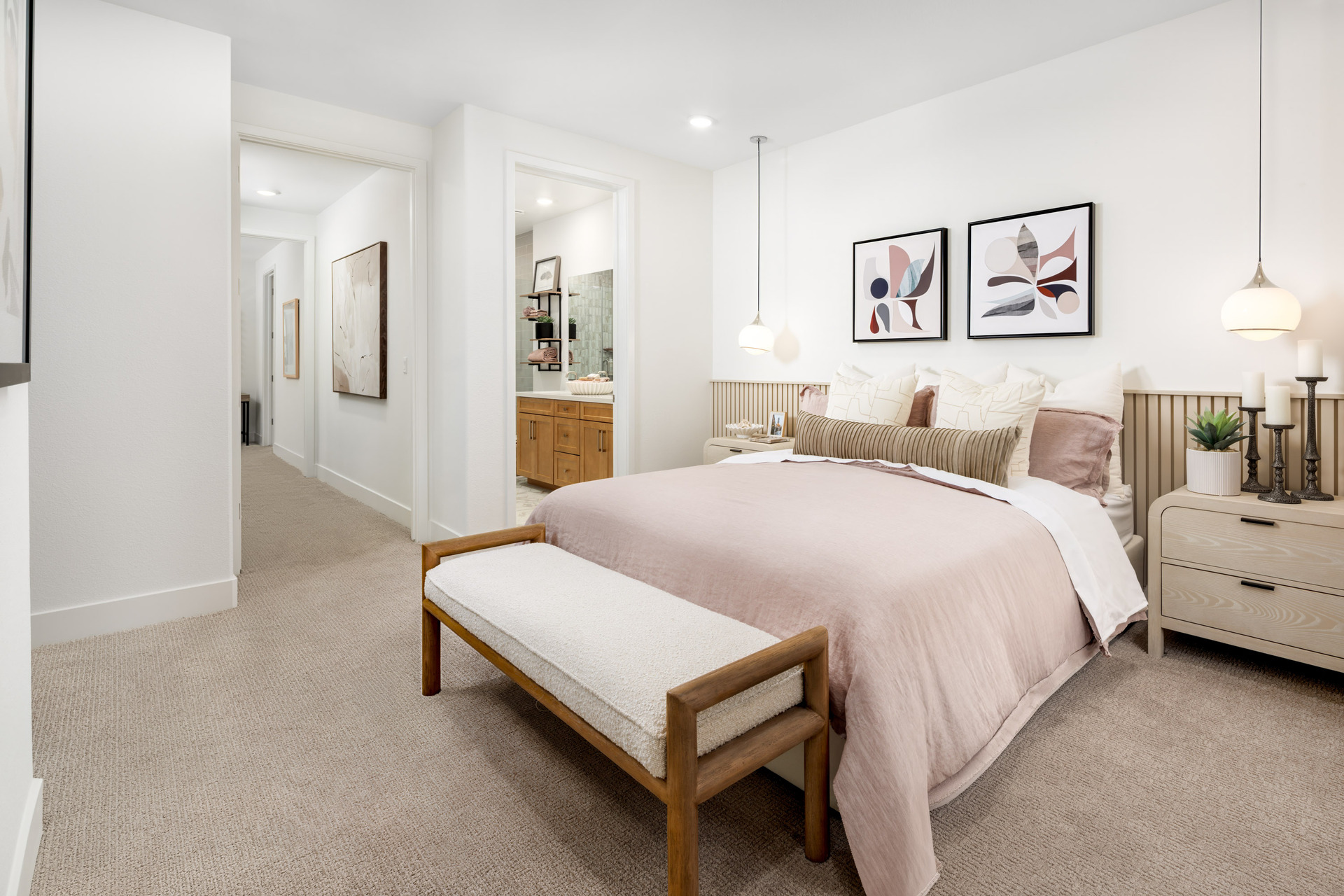 bedroom with tan carpet, blush pink & white bedding, wood bench at foot of bed, and view of attached bathroom