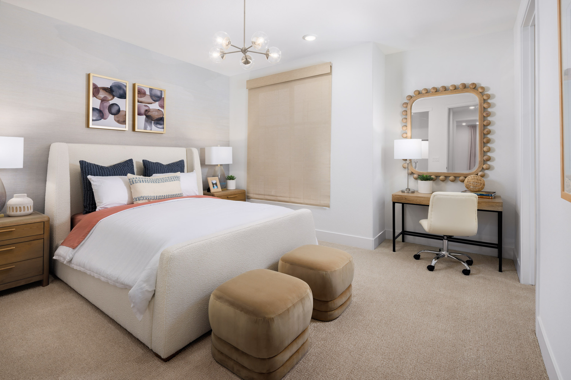 bedroom with tan carpet, mirror above wood desk, and white upholstered bed with two tan velvet ottomans at the foot