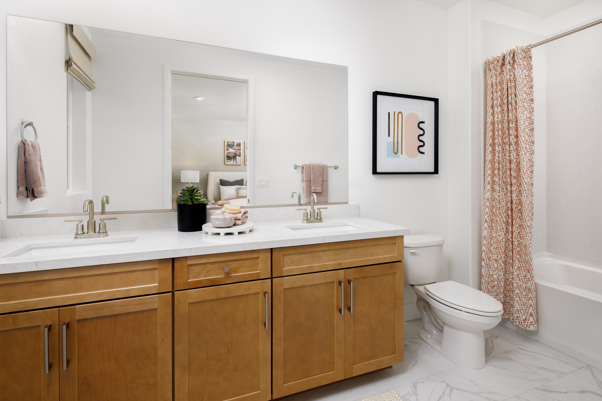 bathroom with light wood cabinets, white counters, two sinks, tub with shower overhead, and orange & white shower curtain