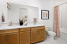 bathroom with light wood cabinets, white counters, two sinks, tub with shower overhead, and orange & white shower curtain