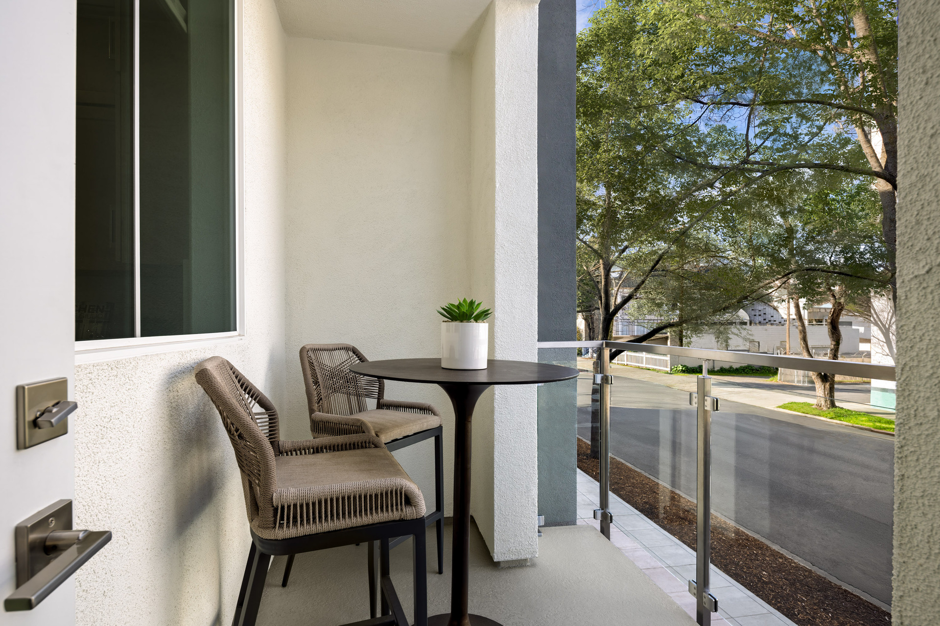 outdoor covered deck with small black pub table and two tan chairs looking out to street