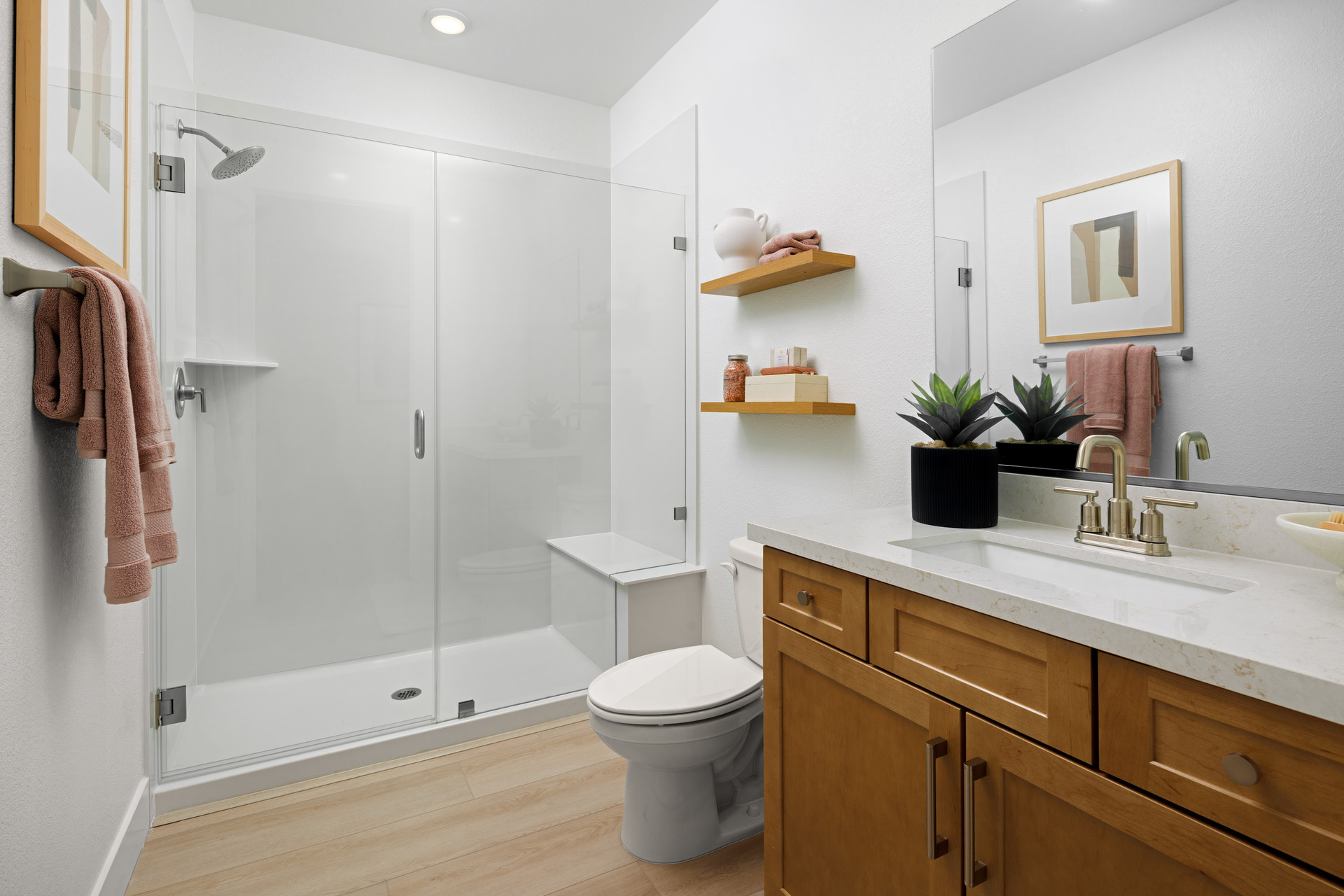 bathroom with light wood cabinets, white counters, large walk-in shower with frameless glass enclosure, and clay-colored towels