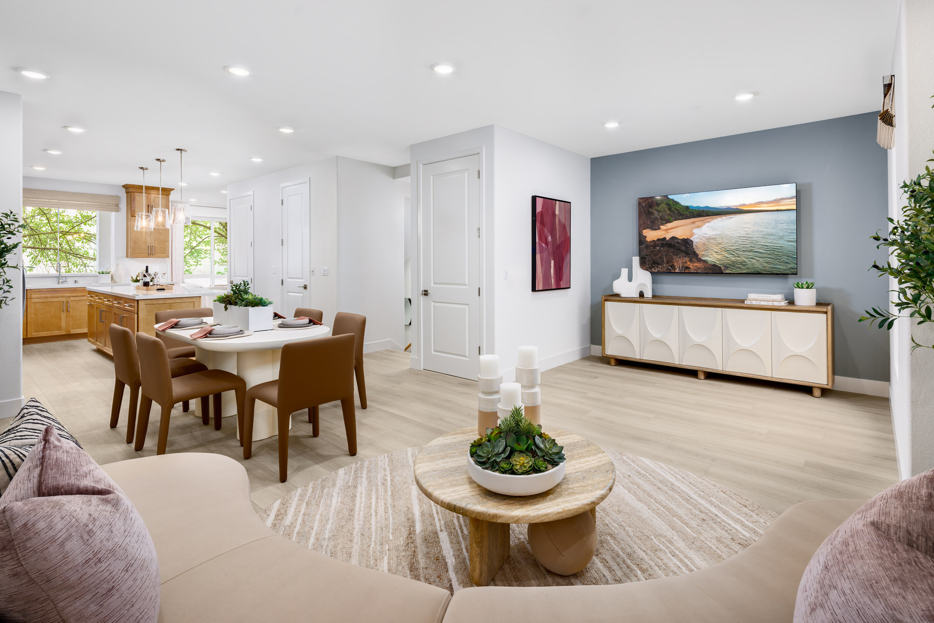great room with light wood floors, slate blue wall behind television, round wood coffee table, and view of dining table with six brown chairs