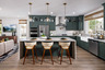 kitchen with green cabinets, white & gray quartz counters, three ivory & wood barstools at island, and window above sink