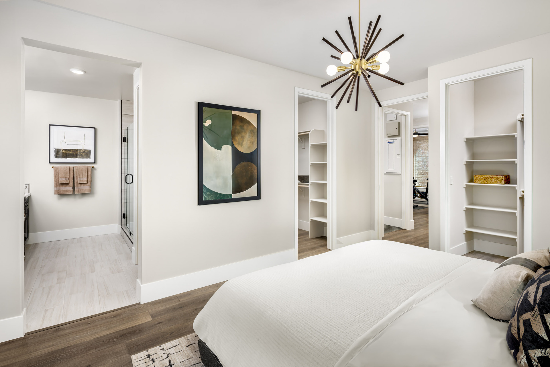 bedroom with wood floors, two walk-in closets, modern black & gold ceiling light fixture, and view of attached bathroom