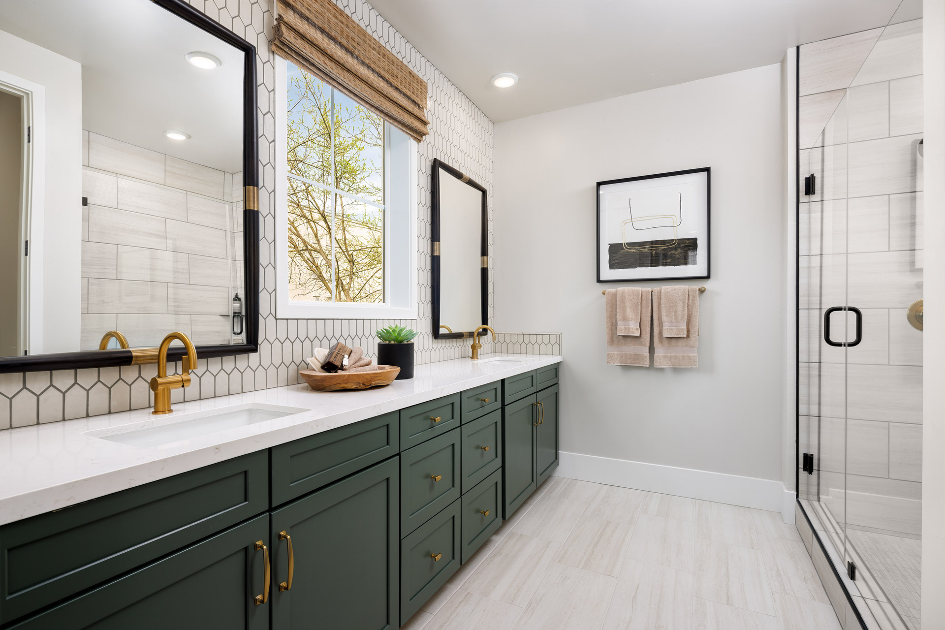 bathroom with green cabinets, white counters, two sinks with gold faucets, window, and large walk-in shower