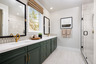 bathroom with green cabinets, white counters, two sinks with gold faucets, window, and large walk-in shower