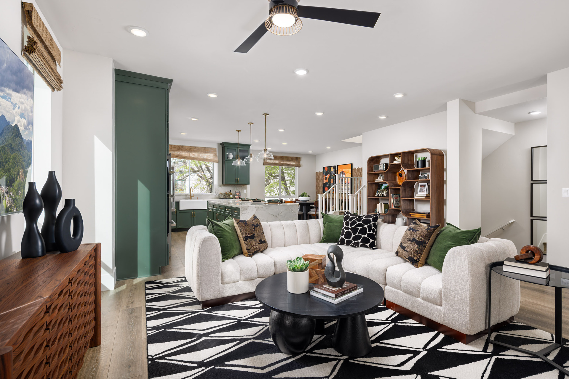great room with black & white patterned area rug, white sectional sofa with green pillows, and round black coffee table
