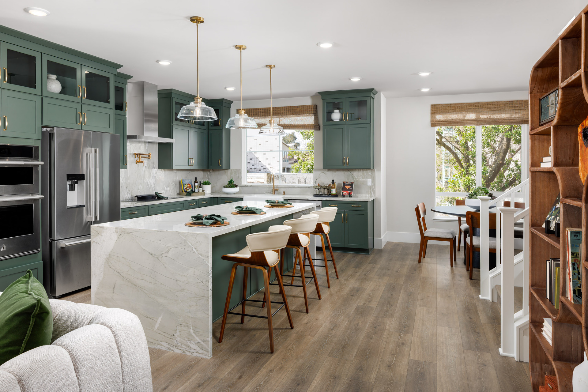 kitchen with green cabinets, light quartz counters, three wood barstools at island, large window by dining table, and window above sink