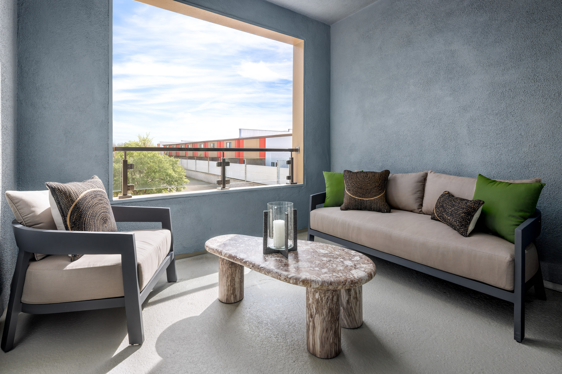 outdoor covered deck with black and tan furniture, and marble looking table with candle in hurricane glass holder