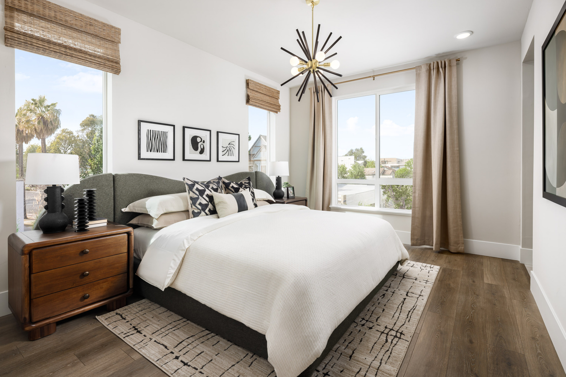 bedroom with wood floors, tan & black area rug, gray upholstered bed, wood nightstands, and multiple windows