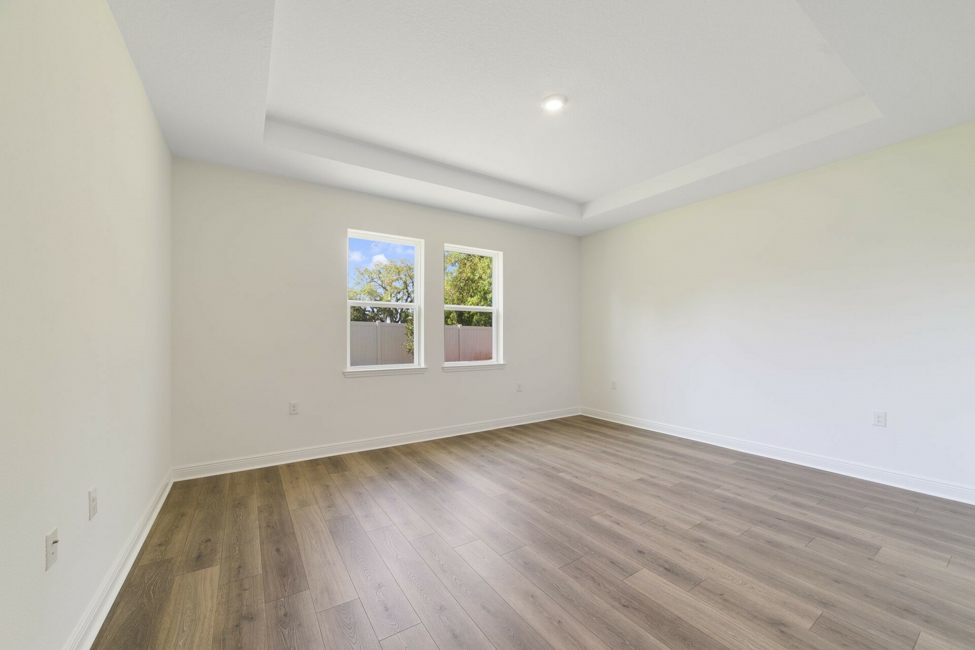 tray ceilings and hardwood vinyl plank with multiple windows. 