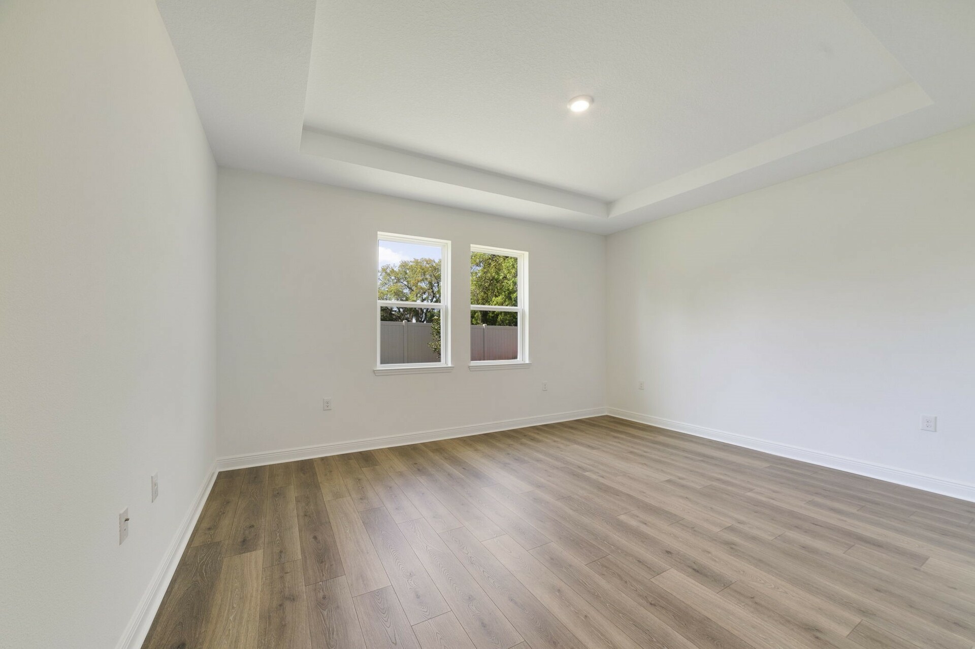 tray ceilings and hardwood vinyl plank with multiple windows. 