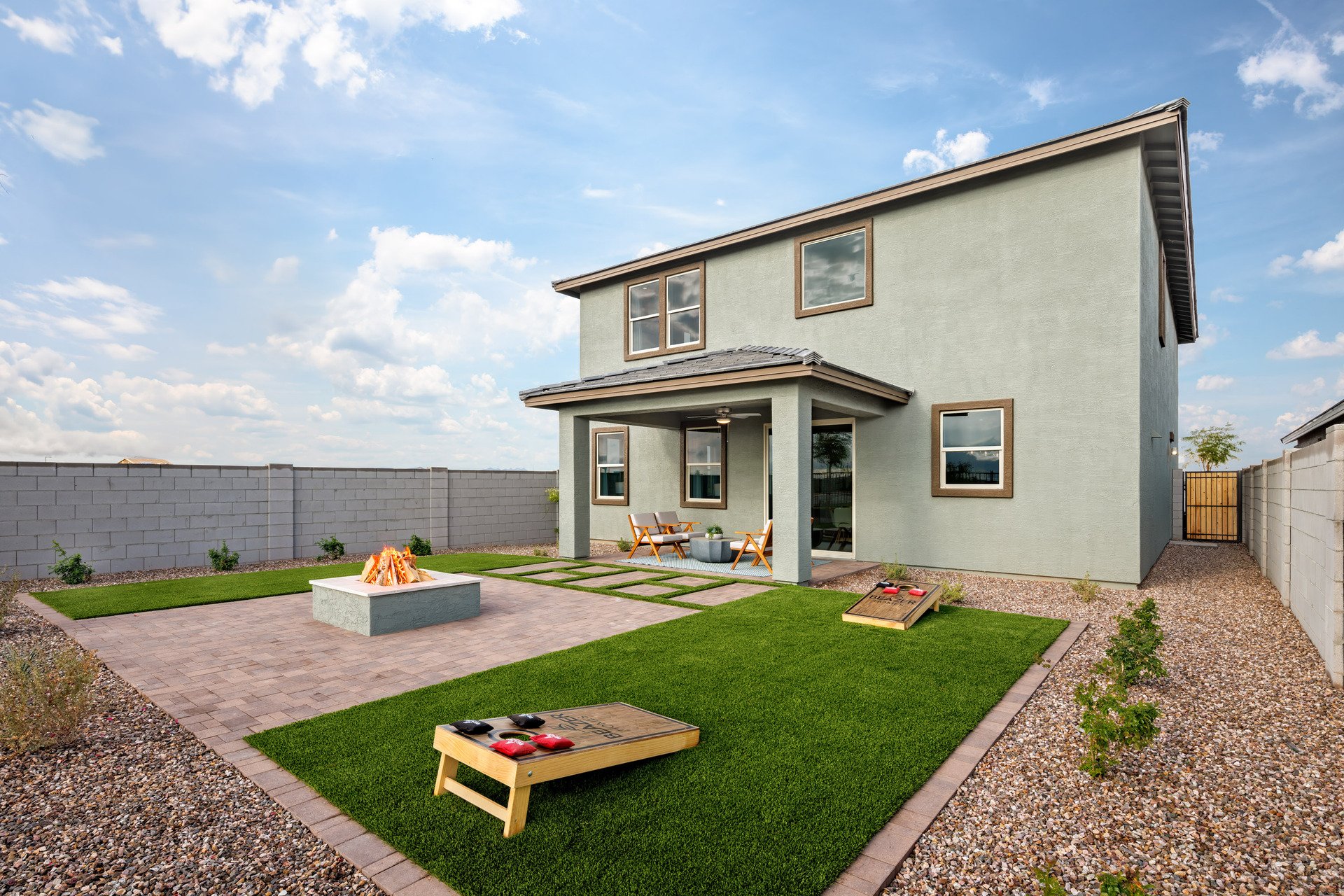 spacious backyard with pavers, artificial grass, a fireplace, and cornhole