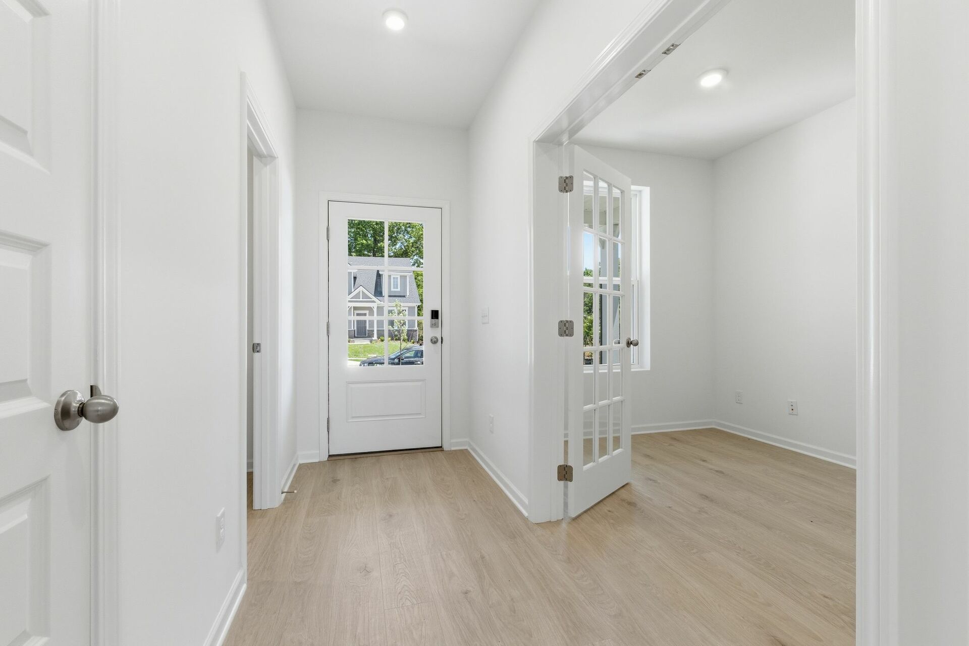 foyer with black entry door, white walls, light wood floor and a study with french doors