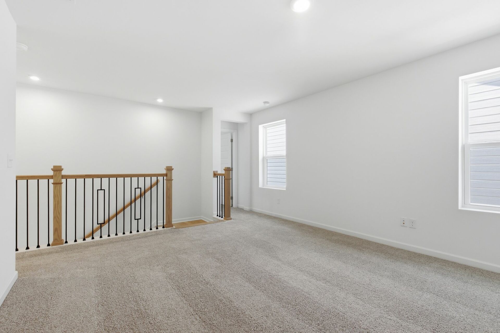 loft with carpet, to windows, and oak tread stairs with iron railing
