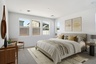 spacious bedroom with a king-sized bed with yellow accent pillows, oak vanity, and grey nightstands