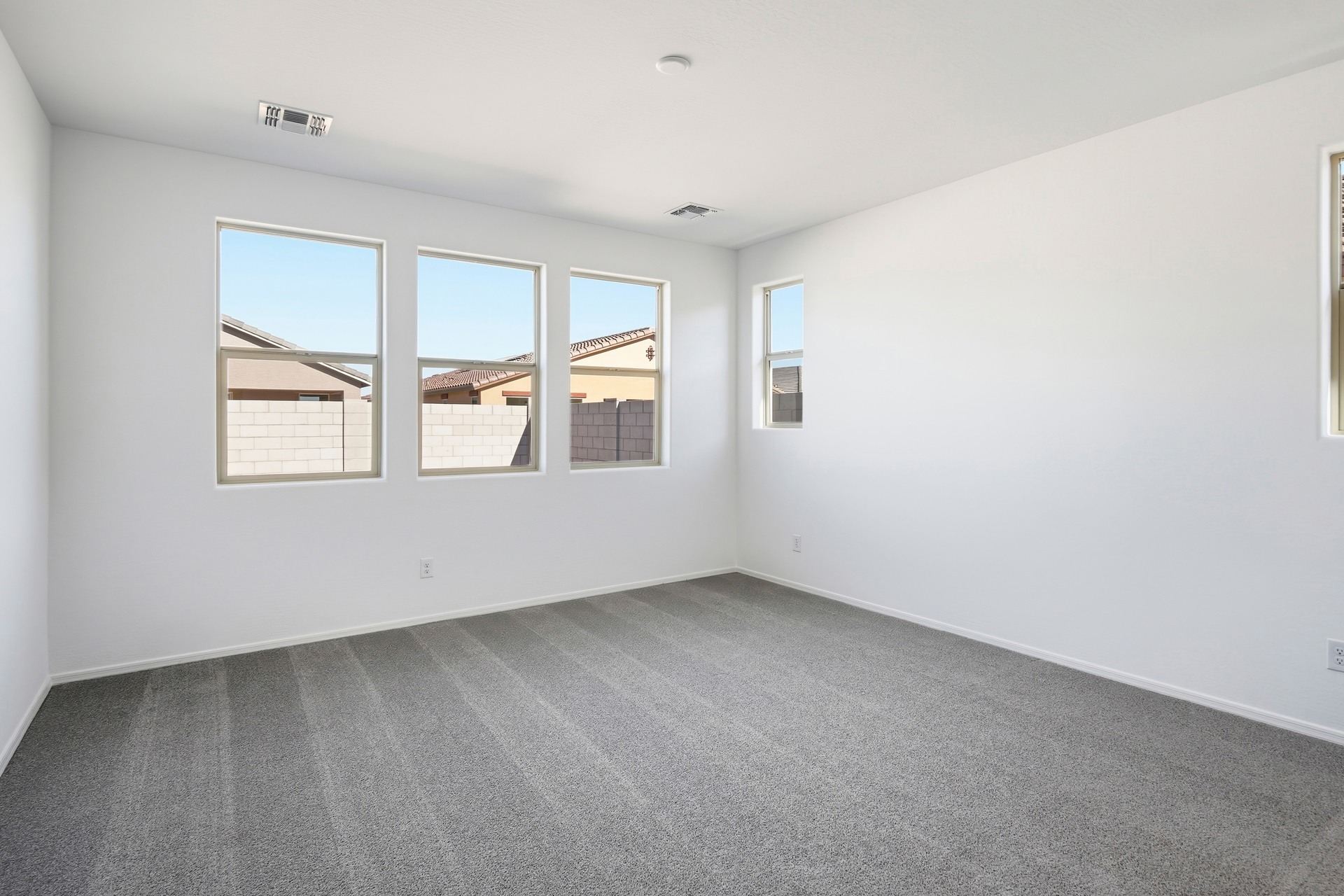 spacious bedroom with light gray carpet and windows for natural light