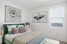 bedroom with green velvet bedframe, white nightstands, and white rug