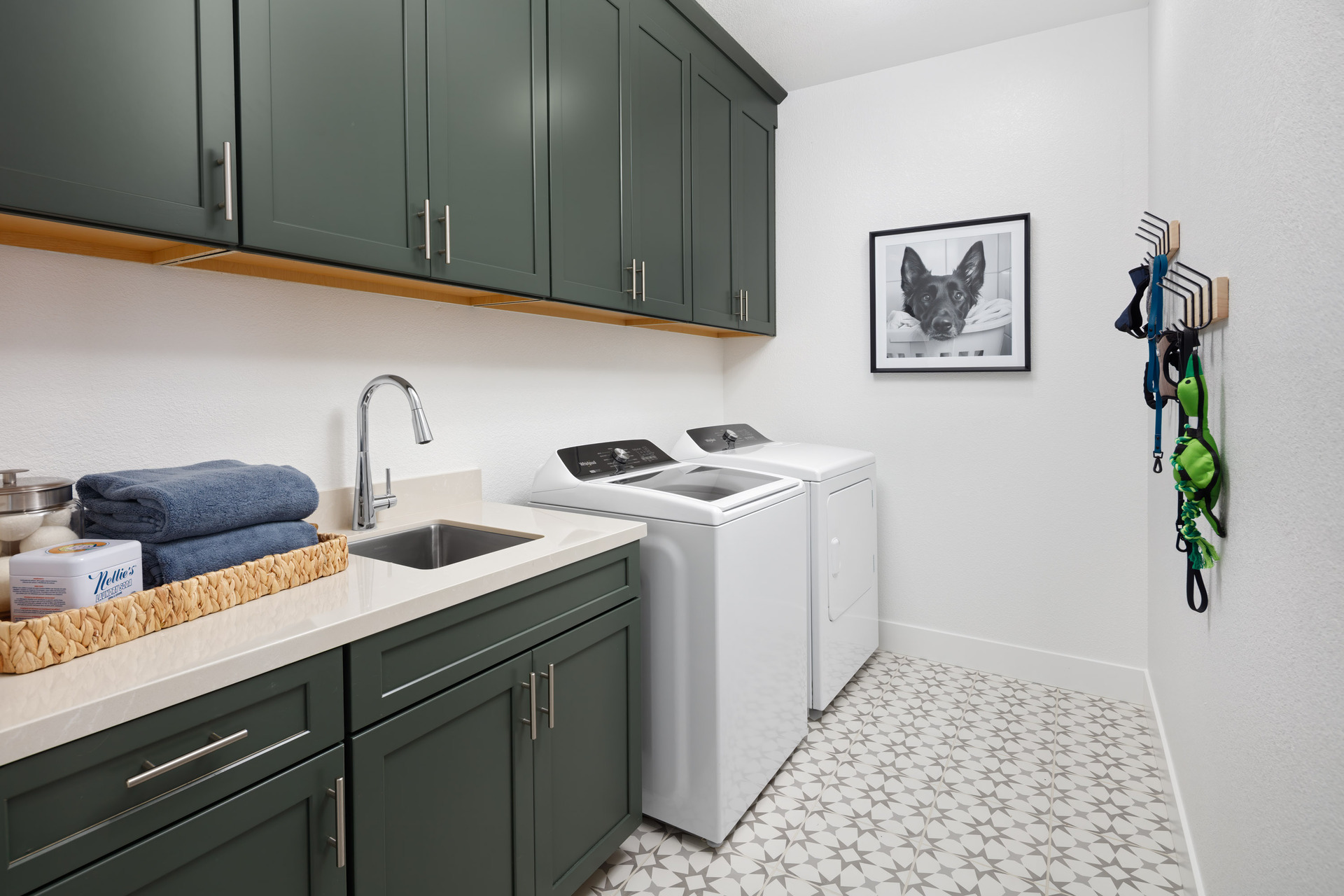 laundry room with olive green upper & lower cabinets, sink, white & gray patterned tile floor and photo of dog on wall