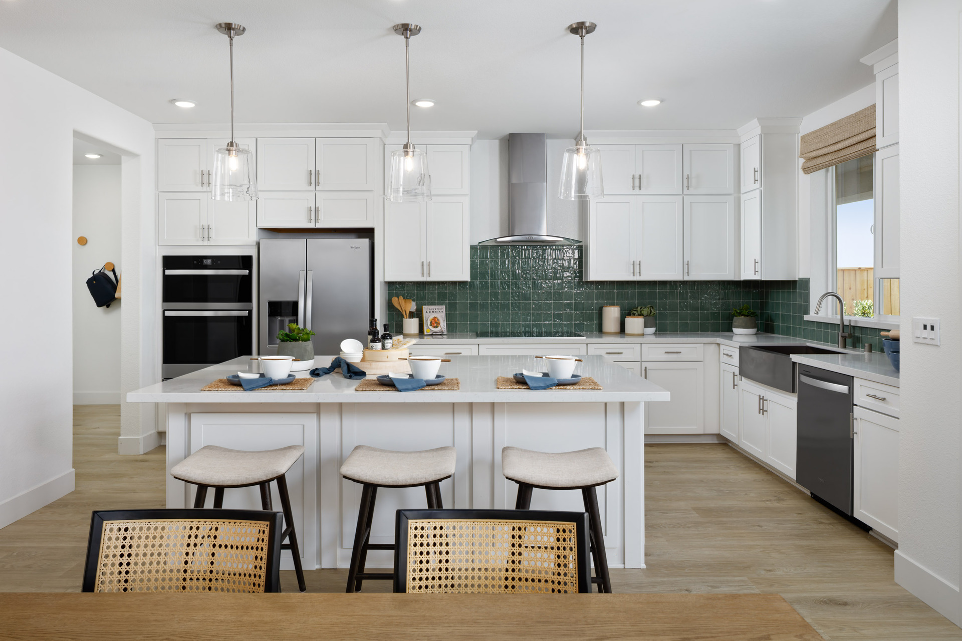 kitchen with white cabinets & counters, wood floors, green tile backsplash, island, stainless steel appliances, and window above sink