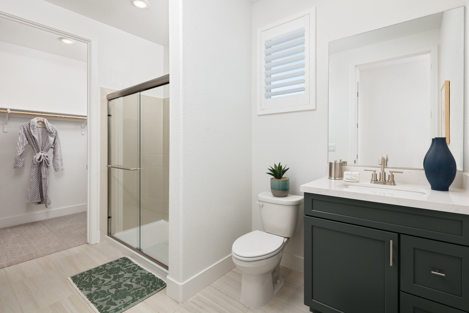 bathroom with olive green cabinets, tan tile floors, shower, walk-in closet, and window above toilet