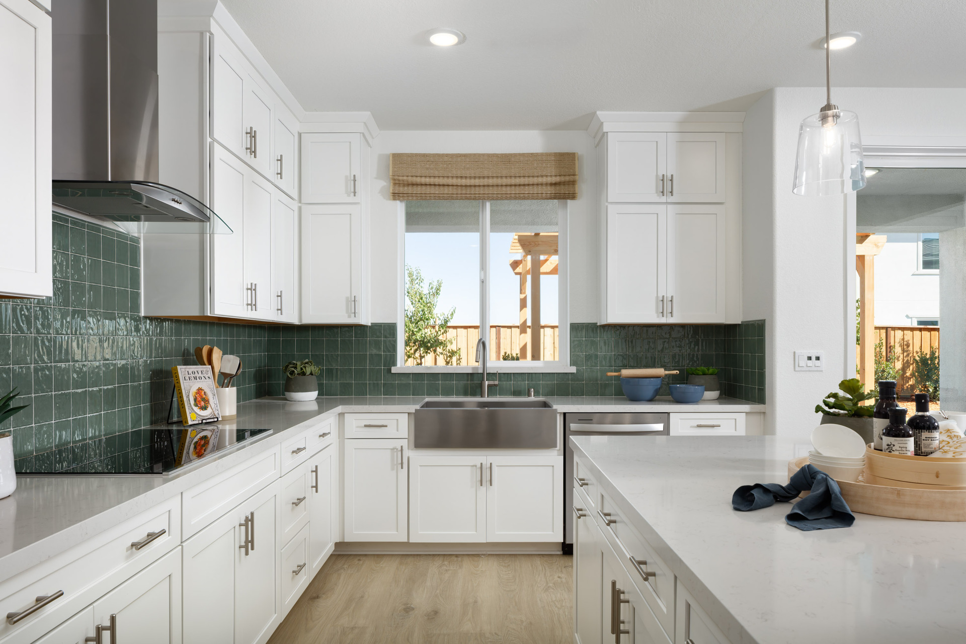 kitchen with white cabinets & counters, green tile backsplash, wood floors, island, and window above sink
